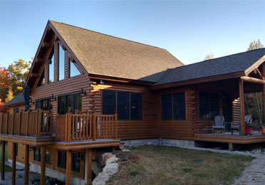 Cedar log home with large windows and wooden deck
