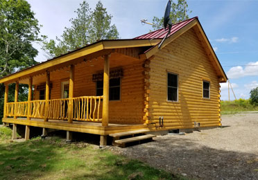 Wooden log cabin with front porch and red roof.