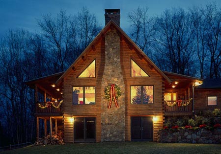 Log home with stone chimney and festive lights at dusk