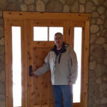 Man standing by a wooden door with stone wall background.