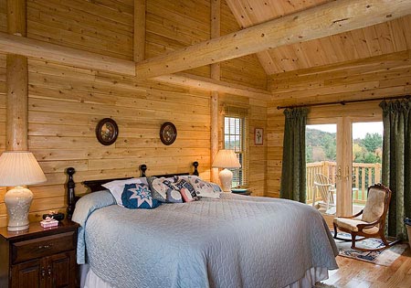 Log cabin bedroom with wooden walls, large bed, and balcony view.