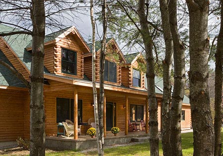 Log home with dormer windows and green roof surrounded by trees