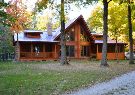 Log home with large windows and autumn trees surrounding it.