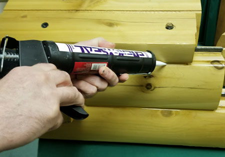 Hands applying caulk to wooden log seam