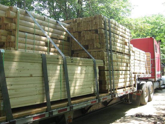 Flatbed truck carrying stacked wooden logs and beams