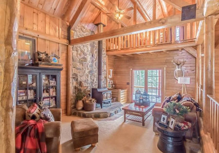 Warm log cabin living room with stone fireplace and wooden beams.
