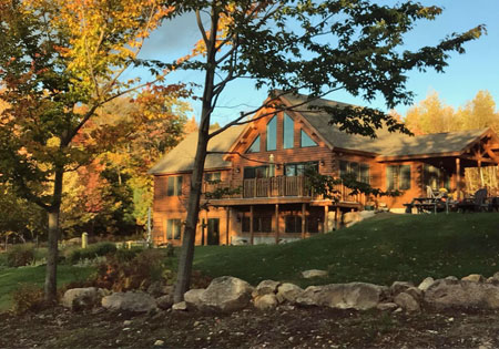 Large log home surrounded by autumn trees and rocks