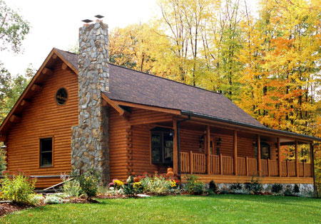 Log home with stone chimney surrounded by autumn trees