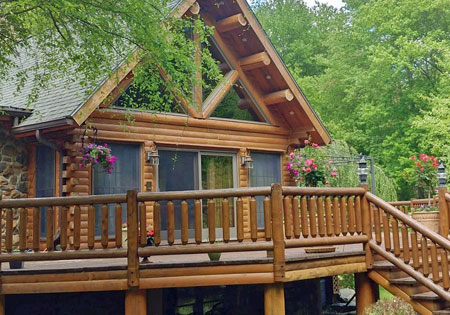 Log cabin with wooden deck surrounded by trees and flowers.