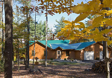 Single-story log home with green roof in autumn forest.