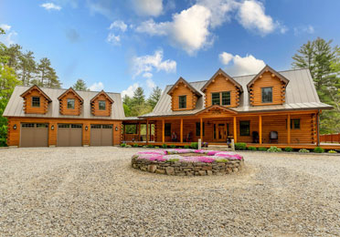 Log home with three-bay garage and stone driveway.