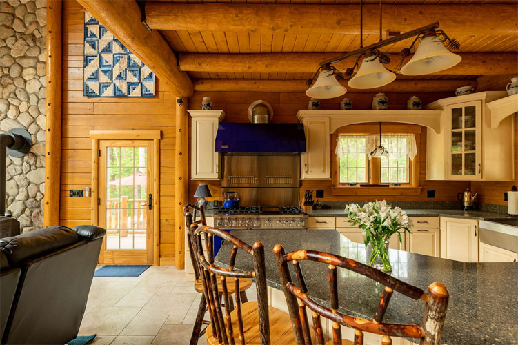 Log home kitchen with wooden beams and stone wall.