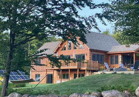 Large log home with solar panels on a grassy hill