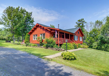 Red log cabin with green roof and lush surroundings