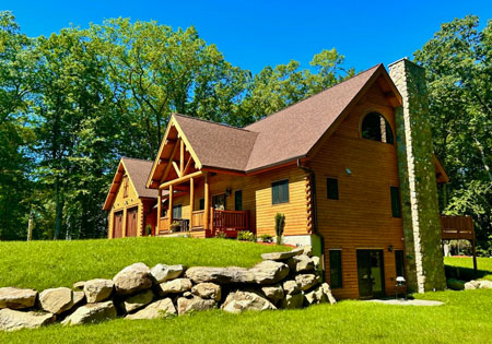 Wooden log cabin with stone chimney surrounded by trees.