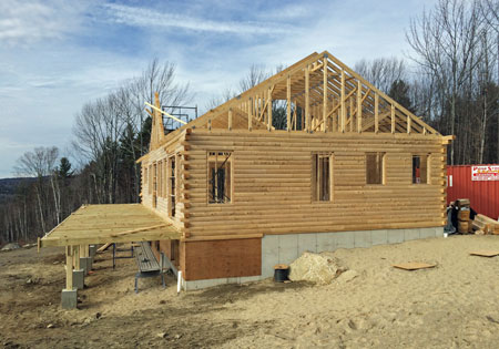 Partially built log home with wooden frame and forest background
