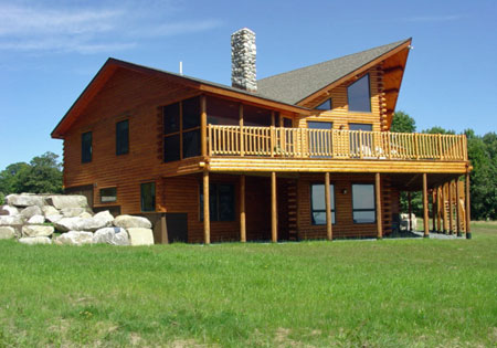 Two-story cedar log home with large balcony and stone chimney.