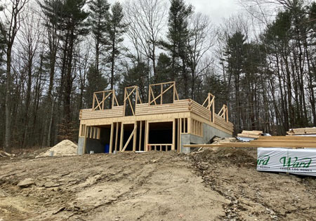 Partially built log home surrounded by trees and construction materials.