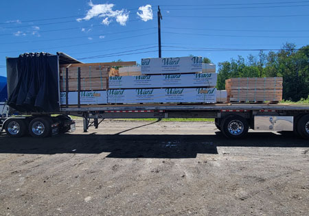 Flatbed truck carrying stacked cedar logs under blue sky