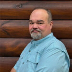 Man in blue shirt posing in front of log wall