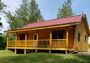Cedar log cabin with red roof and porch in Camp Series package