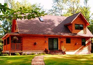 Cedar log home with gabled roof and porch surrounded by trees.