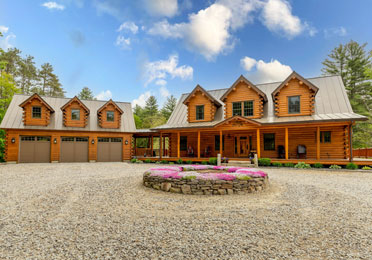 Large cedar log home with three dormers and a garage under a blue sky