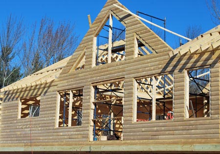 Partially built cedar log home with visible framework and clear sky.