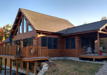Cedar log home with large windows and wooden deck.