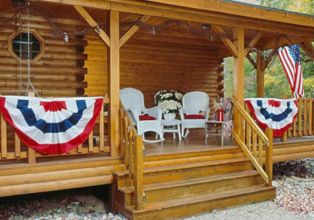 Log home porch with cedar railing, chairs, and patriotic banners.