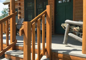 Cedar railings on a wooden porch with chairs and a green door.
