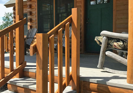 Cedar railings on a wooden porch with chairs and a green door.