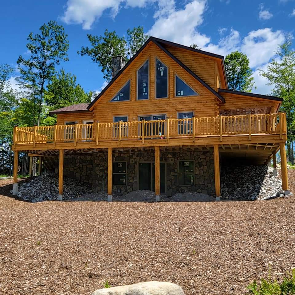 Cedar log home with large wooden deck and stone foundation.