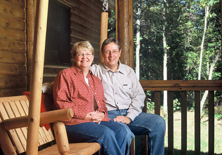 Smiling couple sitting on a wooden porch swing of a log cabin.