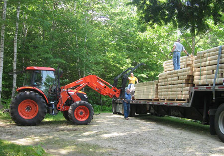 Workers loading cedar logs onto a truck with a tractor.