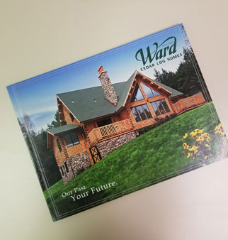 Cedar log home with stone chimney and green roof on grassy hill.