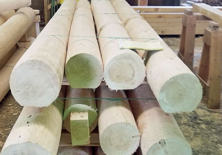 Stack of round wooden joists in a workshop setting.