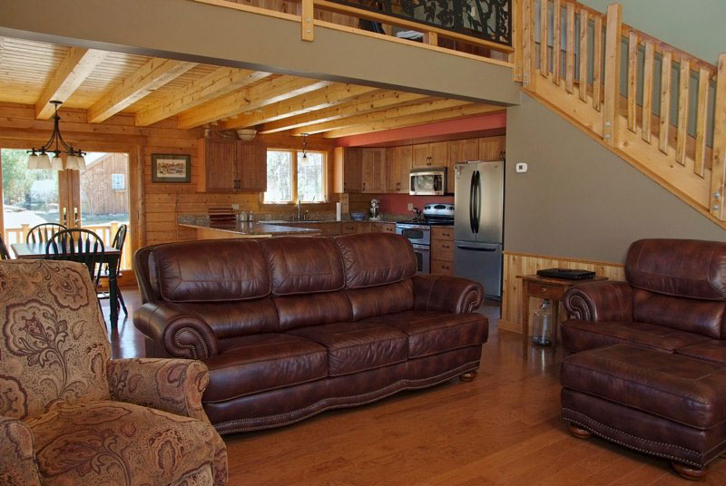 Living room with leather sofas, wooden beams, and staircase.