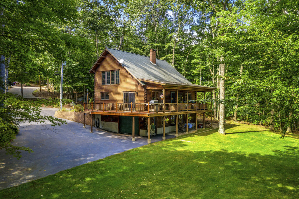 Two-story log home with wraparound porch surrounded by trees