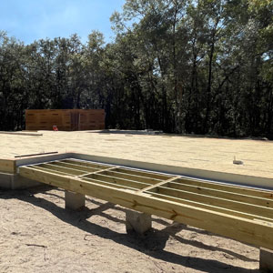 Wooden foundation framework at a log home construction site with trees in the background.
