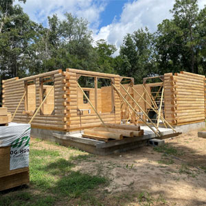 Partially built log home with wooden beams and open sky.