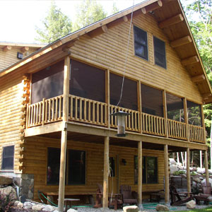 Two-story cedar log home with screened porch and wooden railing.