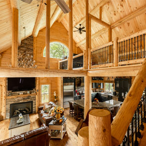 Large open log home interior with loft, wooden beams, and fireplace.