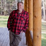 Man in red plaid shirt leaning on log cabin porch