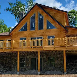 Two-story log home with large windows and stone foundation.