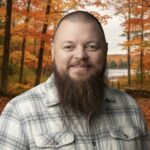 Bearded man in plaid shirt smiling with autumn trees in background