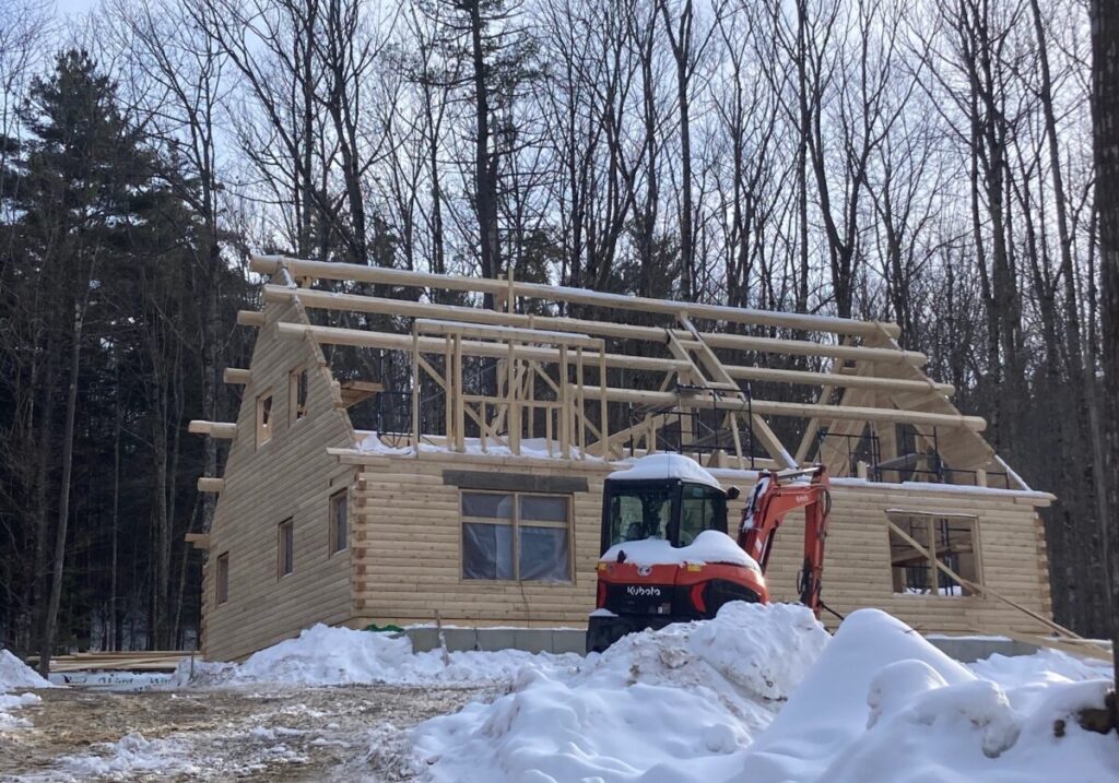 Partially built log home with snow and trees around.