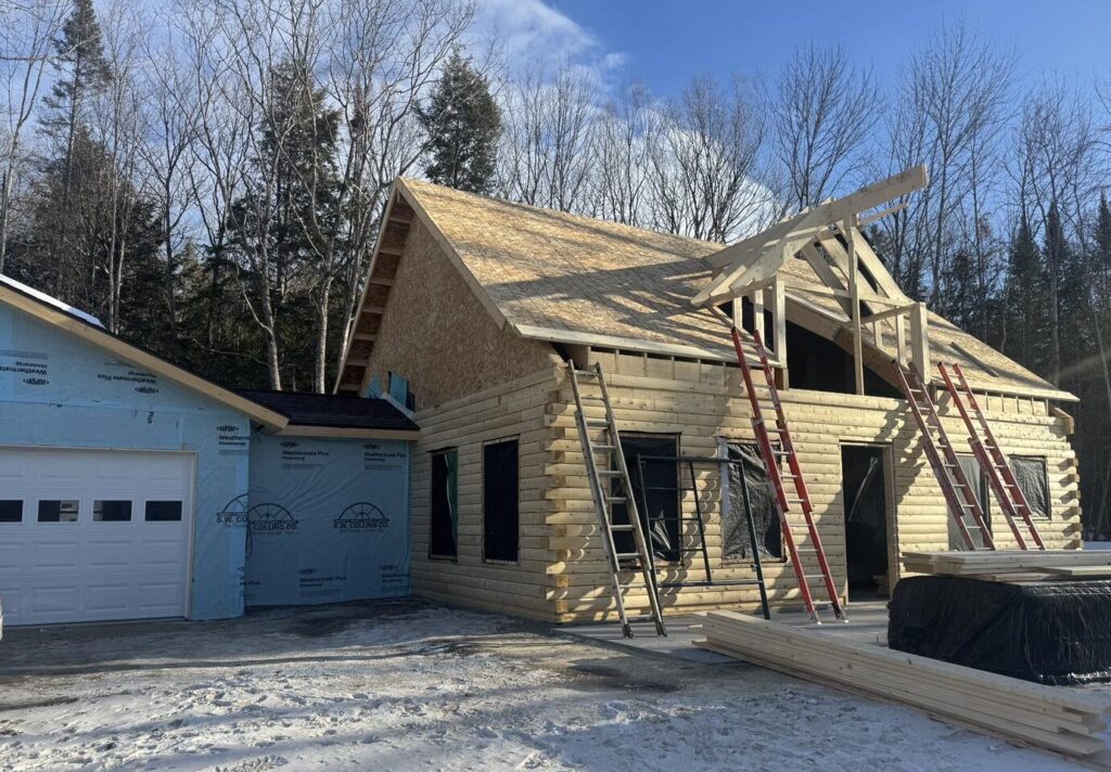 Partially built log home with ladders and snow